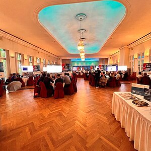 Eleganter Konferenzsaal mit runden Tischen, großen Bildschirmen und Teilnehmern, die sich beim SERVIEW TOOL MEETUP austauschen.