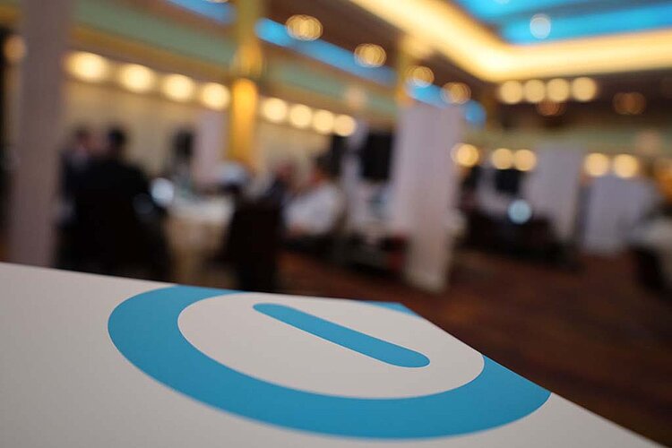 Nahaufnahme des SERVIEW Logos (Blauer Kreis mit blauem Balken in der Mitte) auf einem weißen Stand mit unscharfem Hintergrund einer Konferenzhalle beim SERVIEW TOOL MEETUP.
