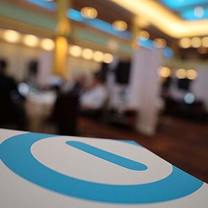 Nahaufnahme des SERVIEW Logos (Blauer Kreis mit blauem Balken in der Mitte) auf einem weißen Stand mit unscharfem Hintergrund einer Konferenzhalle beim SERVIEW TOOL MEETUP.