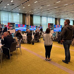 Teilnehmer des SERVIEW TOOL MEETUP24 sitzen an runden Tischen und diskutieren mit Herstellern, während Präsentationen auf großen Bildschirmen gezeigt werden.