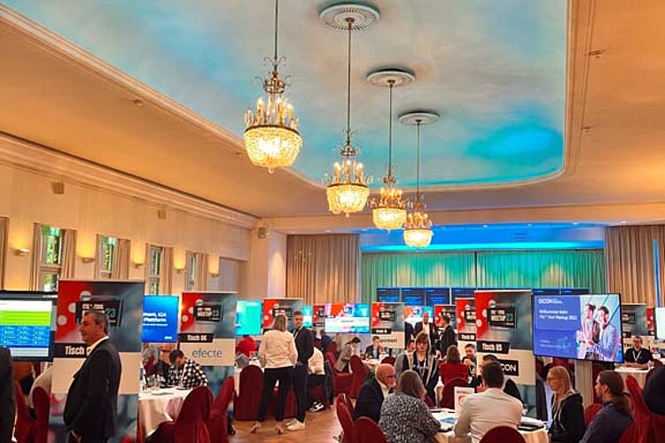 Teilnehmer des SERVIEW TOOL MEETUP sitzen an runden Tischen in einem eleganten Saal mit Kronleuchtern und LED-Deckenbeleuchtung und diskutieren mit Ausstellern.