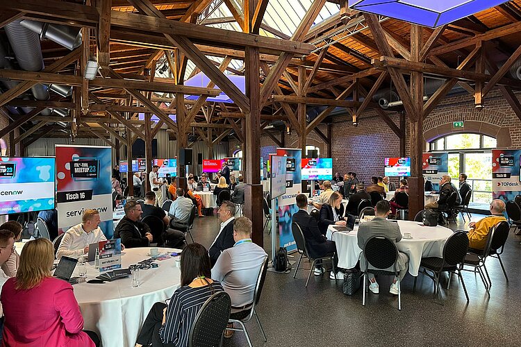 Teilnehmer des SERVIEW TOOL MEETUP23 in einer rustikalen Event-Location mit Holzbalken und Backsteinwänden, die an runden Tischen diskutieren.