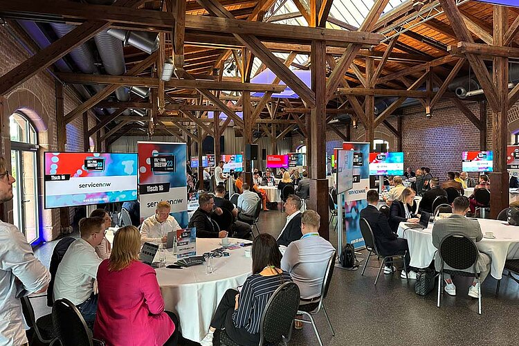 Teilnehmer des SERVIEW TOOL MEETUP23 in einer rustikalen Event-Location mit Holzbalken und Backsteinwänden, die an runden Tischen diskutieren.