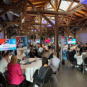 Teilnehmer des SERVIEW TOOL MEETUP23 in einer rustikalen Event-Location mit Holzbalken und Backsteinwänden, die an runden Tischen diskutieren.